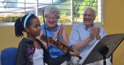 una pareja observa como una niña toca el violín