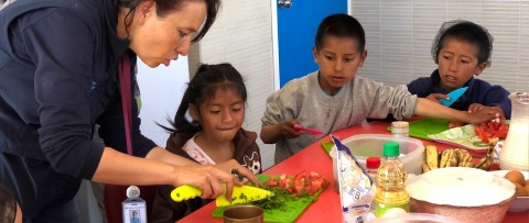 una mujer ayuda a los niños a preparar la comida en una mesa