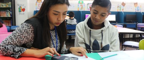 una niña y un niño sentados en una mesa con una calculadora