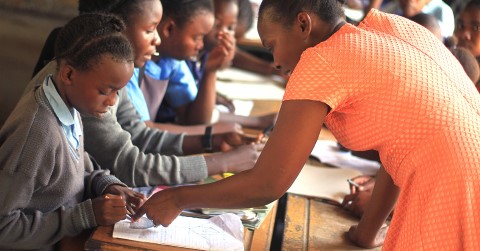 a woman helping a child with a pencil at a desk