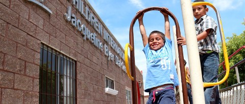 Dos niños jugando en un parque infantil frente al centro comunitario