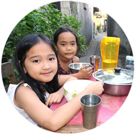 two little girls sitting at a table with a bowl of food