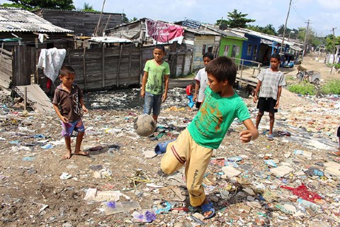 Boys kick a soccer ball among garbage  