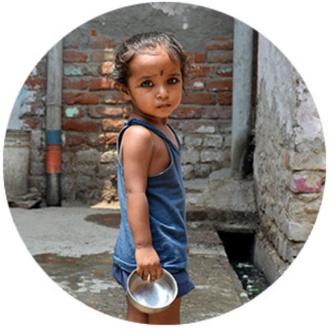 a young girl holding a metal bowl in front of a brick wall