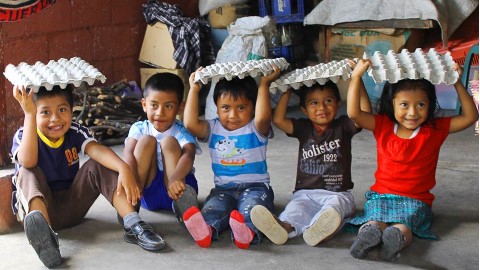 un grupo de niños sentados en el suelo con cartones de huevos en la cabeza