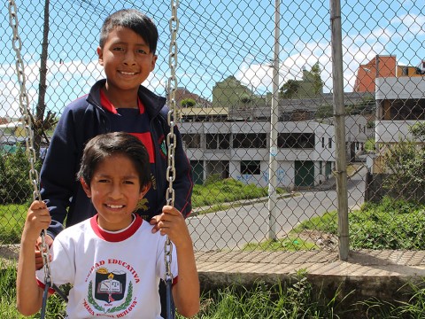 boy sitting on a swing with another boy behind him