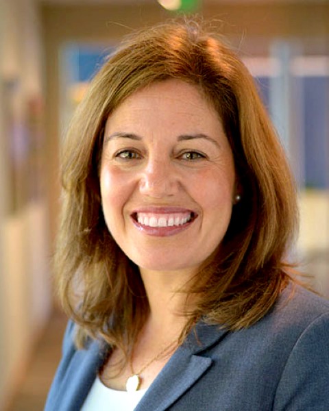 a woman in a grey blazer smiles at the camera