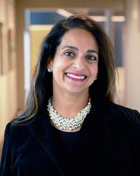 a woman in a black jacket and pearl necklace