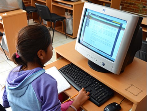 Una niña usa una sala de computación de Children International para leer un artículo en el internet.