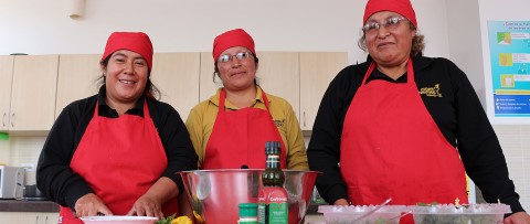 Volunteer mothers with CI’s nutrition program in Ecuador stand in the kitchen with ingredients for salad.