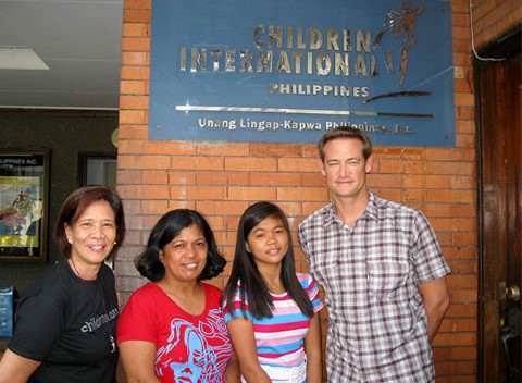 Kent se toma una foto afuera de un centro comunitario con su niña apadrinada, la madre de ella y la directora de la agencia de Children International en Quezon City.