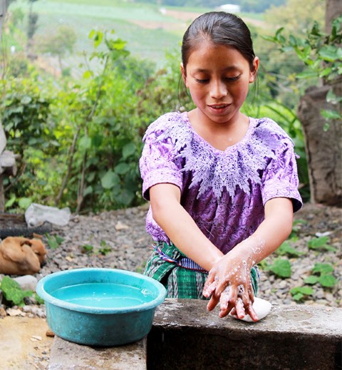 A young girl washes her hands with soap.