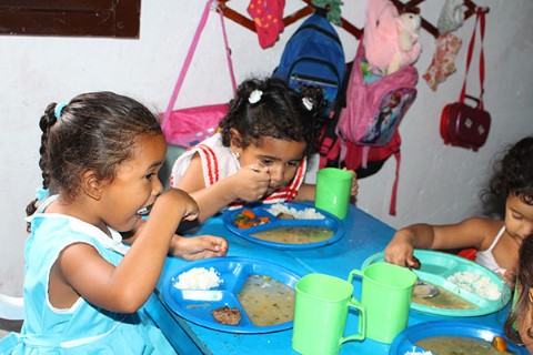 Niñas comen en una pequeña mesa durante el programa de alimentación.