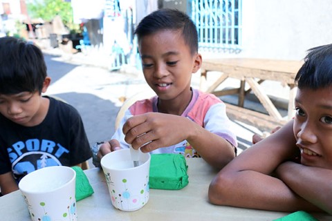 Un niño mezcla leche en una taza de Children International.