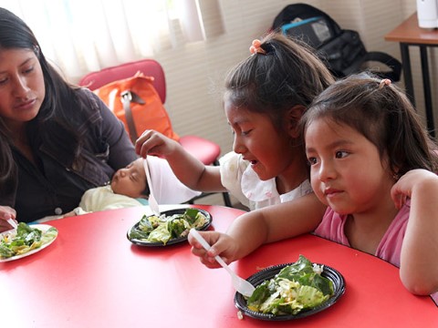 Two young girls from Ecuador sit side by side and try the salad.