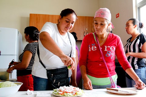 Two mothers prepare a salad and squeeze lime juice on top. 