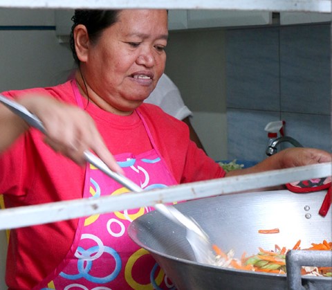 Madre voluntaria mueve una enorme olla de verduras con tallarines. 