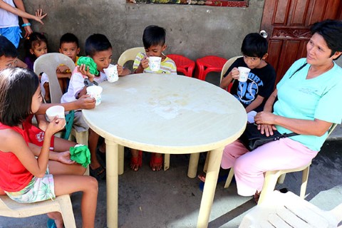 Children eat around a table outside with a volunteer mother.