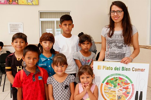 Niños con una voluntaria de Children International sosteniendo el rótulo El Plato del Bien Comer.