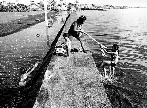 Con su bebé a su costado, una madre ayuda a su hija a subir el malecón.