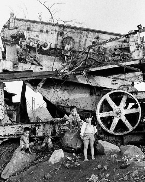 Tres niños juegan en una maquina grande oxidada.