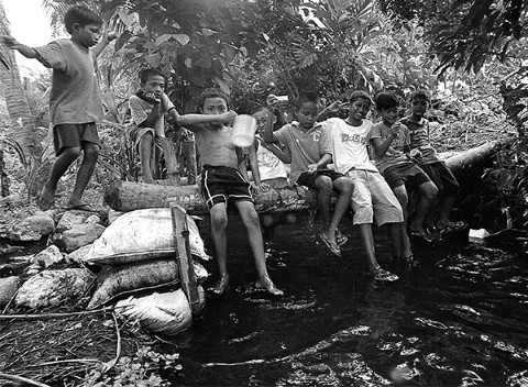 Niños pescan en un arroyo utilizando equipo improvisado.