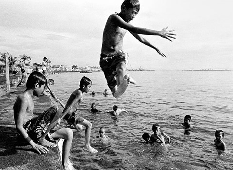 Entre la muchedumbre de nadadores, un niño salta en el océano.