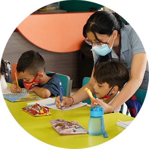 a woman helps two kids studying at a table