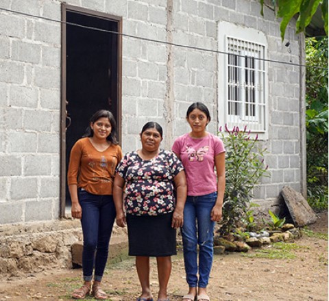 a woman and two young girls standing outside of their home