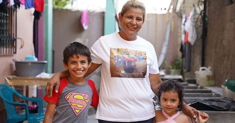 a woman and two kids standing outside of their home